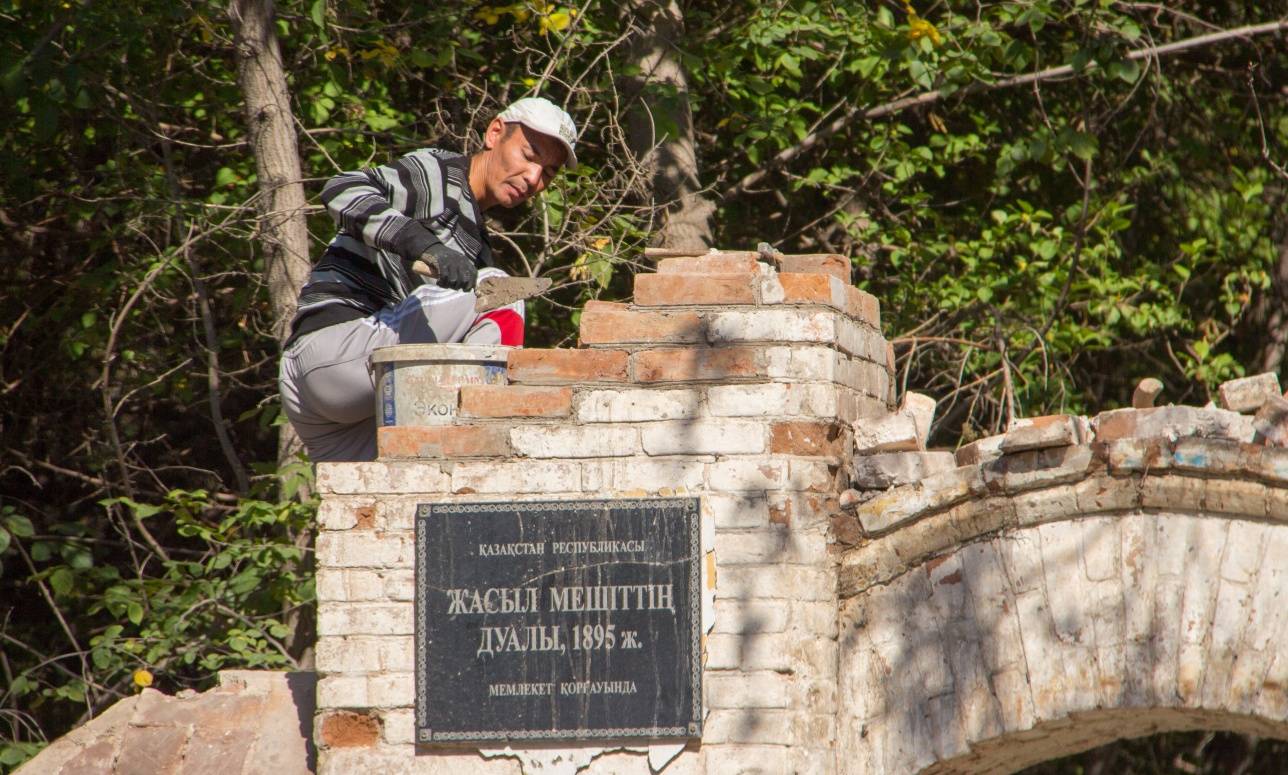 Строители заканчивают укладывать кирпичи на главной арке забора